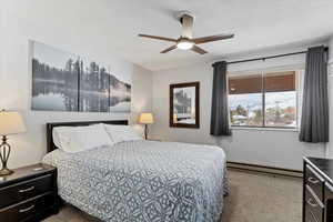 Carpeted bedroom featuring ceiling fan, a textured ceiling, and a baseboard heating unit