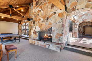 Carpeted living room with beam ceiling, high vaulted ceiling, a stone fireplace, and wood ceiling