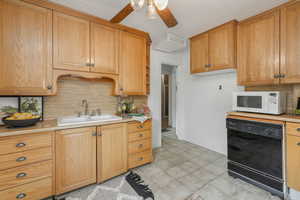 Kitchen featuring sink, decorative backsplash, black dishwasher, and ceiling fan