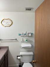 Half bath featuring vanity, visible vents, and toilet