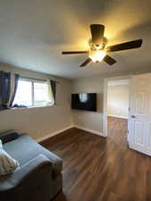 Living room featuring a textured ceiling, ceiling fan, and dark hardwood / wood-style floors