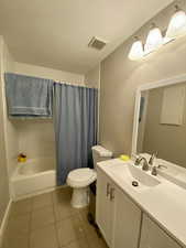 Full bathroom with tile patterned floors, a textured ceiling, vanity, shower / bathtub combination with curtain, and toilet