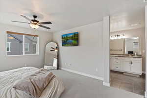 Bedroom featuring connected bathroom, light carpet, a sink, baseboards, and a ceiling fan