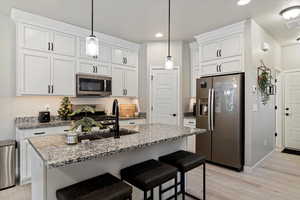 Kitchen with sink, an island with sink, decorative light fixtures, white cabinets, and appliances with stainless steel finishes