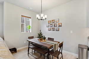 Dining room with light wood finished floors, an inviting chandelier, visible vents, and baseboards