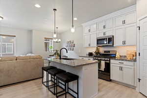 Kitchen featuring a kitchen island with sink, white cabinets, sink, dark stone countertops, and stainless steel appliances