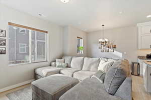 Living area featuring baseboards, visible vents, a notable chandelier, and light wood-style flooring