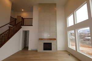 Unfurnished living room with a high ceiling, a healthy amount of sunlight, a large fireplace, and light hardwood / wood-style flooring