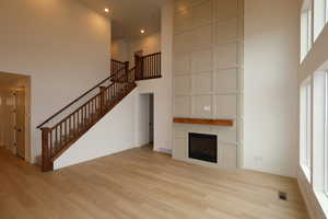 Unfurnished living room with light wood-type flooring, a large fireplace, and a high ceiling