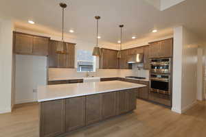 Kitchen featuring sink, appliances with stainless steel finishes, decorative backsplash, a kitchen island, and decorative light fixtures