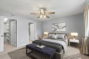 Carpeted bedroom featuring a walk in closet, en suite bathroom and ceiling fan.  Virtually staged to enhance the possibilities of this large room.