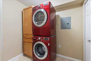 Washroom with electric panel, cabinets, and stacked washer and clothes dryer