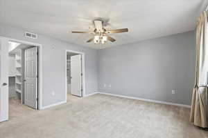 Unfurnished view of primary bedroom featuring ceiling fan, a spacious closet, light carpet, and an en suite bathroom.