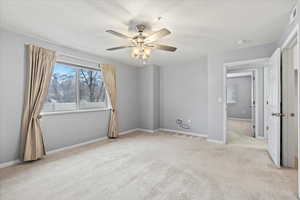 Unfurnished view of primary bedroom featuring ceiling fan, a spacious closet, light carpet, and an en suite bathroom.