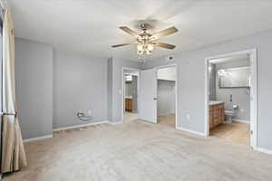 Unfurnished view of primary bedroom featuring ceiling fan, a spacious closet, light carpet, and an en suite bathroom.