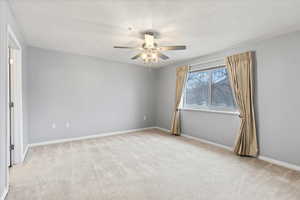 Unfurnished view of primary bedroom featuring ceiling fan, a spacious closet, light carpet, and an en suite bathroom.