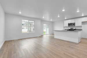 Kitchen featuring white cabinetry, sink, light hardwood / wood-style floors, a center island with sink, and appliances with stainless steel finishes