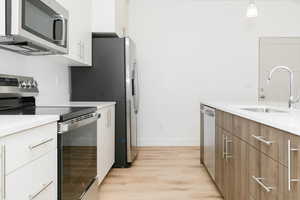 Kitchen featuring white cabinets, sink, hanging light fixtures, light hardwood / wood-style flooring, and stainless steel appliances