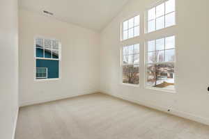 Carpeted spare room featuring vaulted ceiling