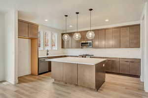 Kitchen with appliances with stainless steel finishes, sink, hanging light fixtures, a center island, and light hardwood / wood-style flooring