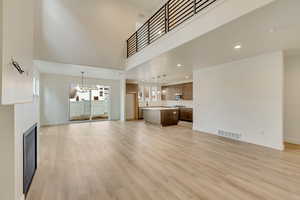 Unfurnished living room featuring a towering ceiling, a chandelier, and light hardwood / wood-style flooring