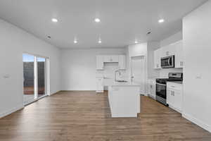 Kitchen with sink, wood-type flooring, a kitchen island with sink, white cabinets, and appliances with stainless steel finishes