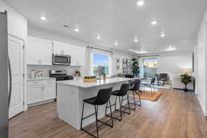 Kitchen featuring white cabinetry, stainless steel appliances, a kitchen breakfast bar, a kitchen island, and light wood-type flooring