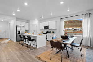 Kitchen with a breakfast bar, a kitchen island with sink, appliances with stainless steel finishes, light hardwood / wood-style floors, and white cabinetry