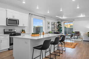 Kitchen featuring white cabinets, an island with sink, appliances with stainless steel finishes, a tray ceiling, and wood-type flooring