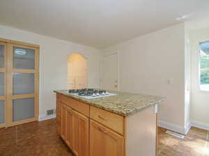 Kitchen featuring light stone countertops, light brown cabinets, a center island, and white gas cooktop