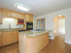 Kitchen featuring light stone counters, white gas cooktop, a kitchen island, sink, and oven