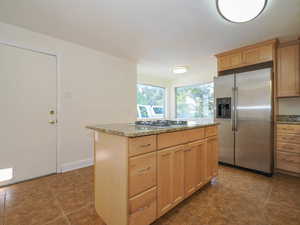 Kitchen featuring a center island, white gas stovetop, stainless steel refrigerator with ice dispenser, and light brown cabinetry