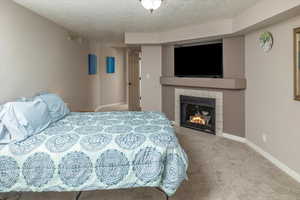 Carpeted bedroom with a textured ceiling and a tiled fireplace