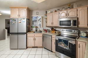 Kitchen featuring light brown cabinets, stainless steel appliances, light tile patterned floors, and sink