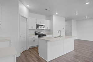 Kitchen with sink, light hardwood / wood-style flooring, an island with sink, white cabinets, and appliances with stainless steel finishes