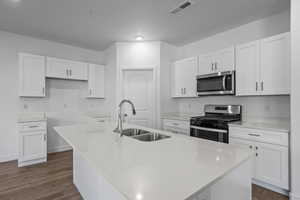 Kitchen with a kitchen island with sink, sink, white cabinets, and appliances with stainless steel finishes