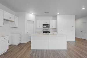 Kitchen with white cabinetry, a kitchen island with sink, sink, and appliances with stainless steel finishes