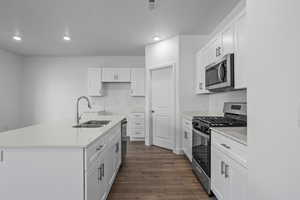 Kitchen featuring white cabinets, appliances with stainless steel finishes, sink, and an island with sink