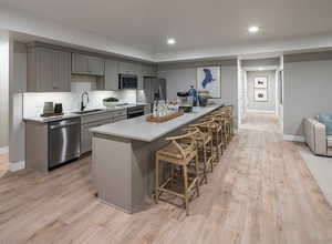 Kitchen featuring gray cabinetry, a breakfast bar, stainless steel appliances, and light hardwood / wood-style flooring