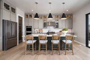 Kitchen with stainless steel appliances, gray cabinets, hanging light fixtures, and an island with sink