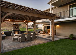 Patio terrace at dusk with an outdoor living space with a fireplace, a balcony, a pergola, and a lawn