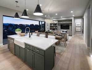 Kitchen with built in shelves, sink, decorative light fixtures, light hardwood / wood-style floors, and an island with sink