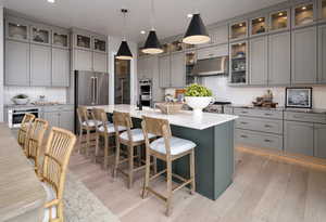 Kitchen featuring high end refrigerator, light wood-type flooring, gray cabinetry, decorative light fixtures, and a center island with sink