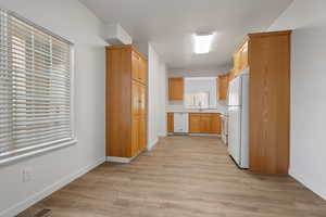 Kitchen with light wood-type flooring, light brown cabinets, white appliances, and sink