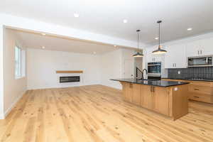 Kitchen with a breakfast bar, stainless steel appliances, decorative light fixtures, a center island with sink, and white cabinets