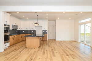 Kitchen with a center island with sink, light wood-type flooring, appliances with stainless steel finishes, decorative light fixtures, and white cabinetry