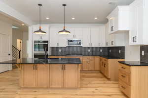 Kitchen with pendant lighting, a center island with sink, light hardwood / wood-style floors, white cabinetry, and stainless steel appliances