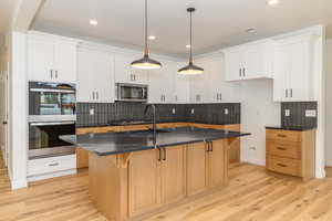 Kitchen with white cabinets, an island with sink, decorative light fixtures, and appliances with stainless steel finishes