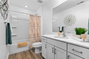 Full bathroom with hardwood / wood-style flooring, vanity, shower / bath combination with curtain, and toilet