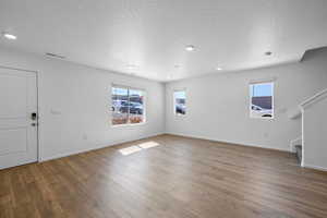 Unfurnished living room with a wealth of natural light, wood-type flooring, and a textured ceiling